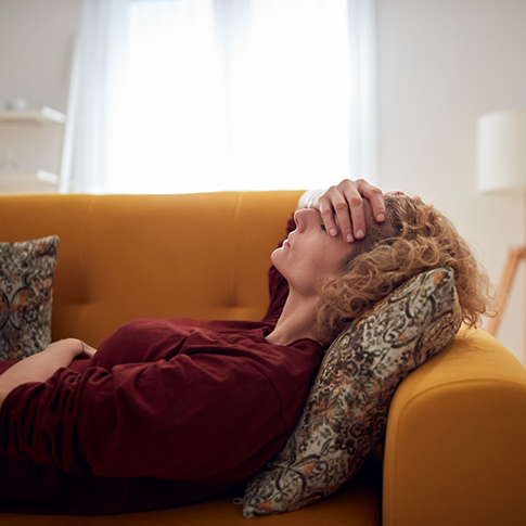 Woman laying on a couch and holding her forehead in her hand
